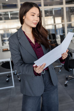 Smiling young woman holding documents in hands and looking contented