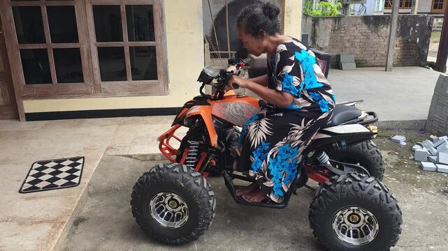 An adult woman sitting on an orange all terrain vehicle parked in the yard checking the controls