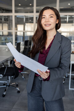 Smiling young woman holding documents in hands and looking contented