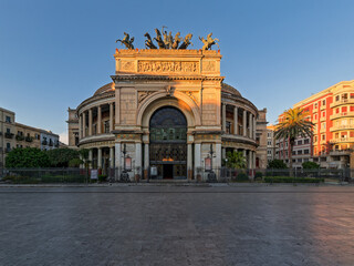 Fototapeta premium Majestic Politeama Garibaldi theater in Palermo, Italy. Beautiful warm sunset light illuminating the grand triumphal arch and bronze chariot statue on an empty European plaza.