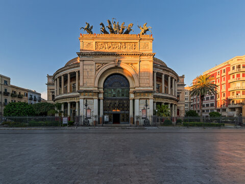Majestic Politeama Garibaldi theater in Palermo, Italy. Beautiful warm sunset light illuminating the grand triumphal arch and bronze chariot statue on an empty European plaza.
