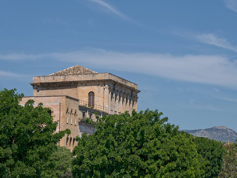 Classic Sicilian architecture over the historic Porta dei Greci gate in Palermo, Sicily. Tiled roof building framed by tropical trees and palm fronds, perfect for travel editorial.
