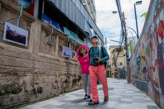 People walking in a colorful alley with street art and photos hanging on the walls during a sunny day