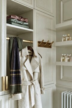 Cream painted Parisian walk-in wardrobe corner featuring a stylish coat, scarves, and neatly arranged perfume bottles on shelves with elegant design elements