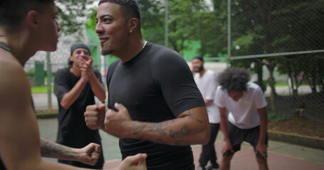Naklejka premium Hispanic and African descent men celebrating score on outdoor basketball court, shouting with joy and energy after intense game, team unity and streetball spirit