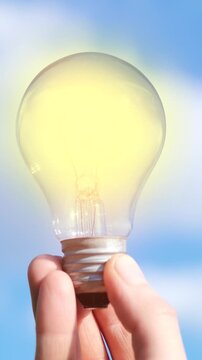 Close-up of a flickering glowing light bulb held against blue sky. Symbol of ideas, innovation, unstable electricity, inspiration, creativity and renewable energy