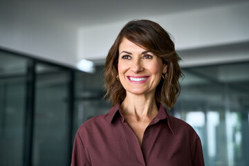 Fototapeta premium Looking aside at copy space, smiling hispanic businesswoman poses for close up portrait in office. Happy mature woman face expresses joy. Dreaming female business leader imagines company vision.