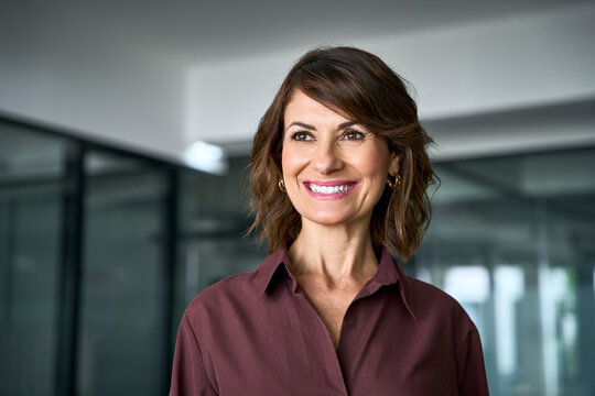 Looking aside at copy space, smiling hispanic businesswoman poses for close up portrait in office. Happy mature woman face expresses joy. Dreaming female business leader imagines company vision.