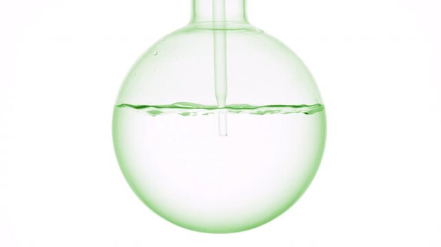 Closeup shot of colorless transparent liquid injected through a long dropper into a round-bottom flask causing swirls and bubbles on neutral white surface | Make-up remover visual advertising concept