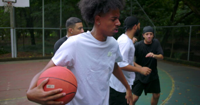 Hispanic men arguing during street basketball game as African descent player steps in to de-escalate conflict, intense emotions and confrontation on court