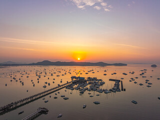 Naklejka premium A breathtaking aerial view of Chalong Bay Marina in Phuket, Thailand, captured during sunrise with golden reflections across the calm Andaman Sea and hundreds of anchored boats.
