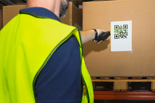Close-up of a warehouse worker scanning a QR code on a cardboard box using a handheld scanner
