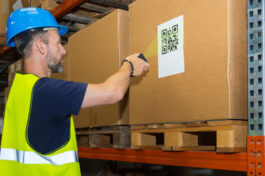 Side view of a warehouse worker in a blue hard hat scanning a QR code on a box