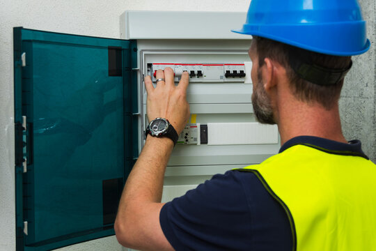 Close-up of an electrician in a blue hard hat checking a fuse box panel