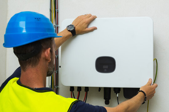 Technician in a blue hard hat installing a solar inverter on a wall