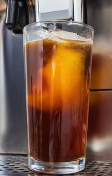 Fresh iced coffee with ice cubes in a tall glass inside an espresso coffee machine