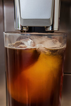 Close-up of black coffee pouring into a glass filled with ice cubes from a coffee machine