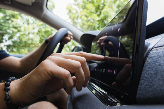 Close-up of a driver's hand touching the infotainment navigation screen on a car dashboard while driving