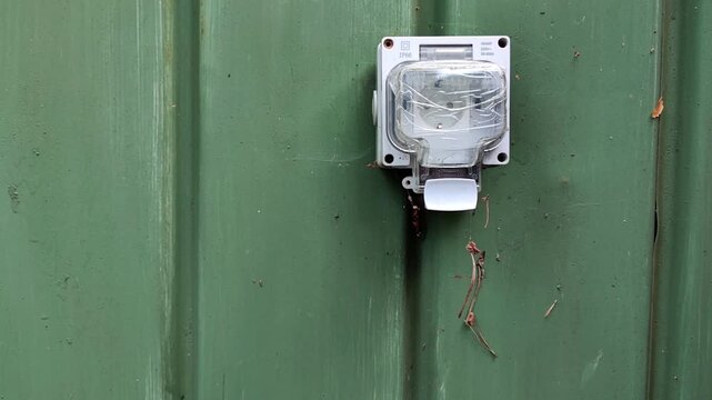 Outdoor electric meter mounted on a green wall, residential utility equipment, infrastructure, technical installation.