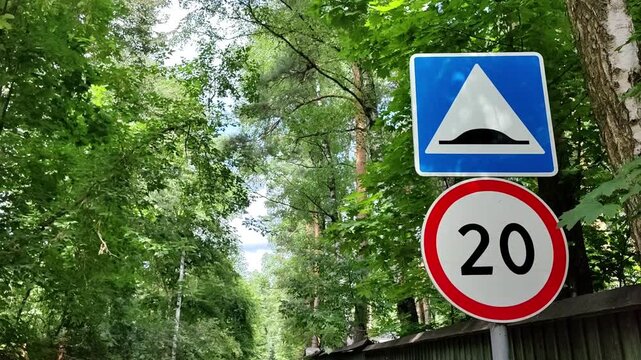 Traffic signs showing speed limit and speed bump warning on a quiet forest road, safe residential neighborhood.