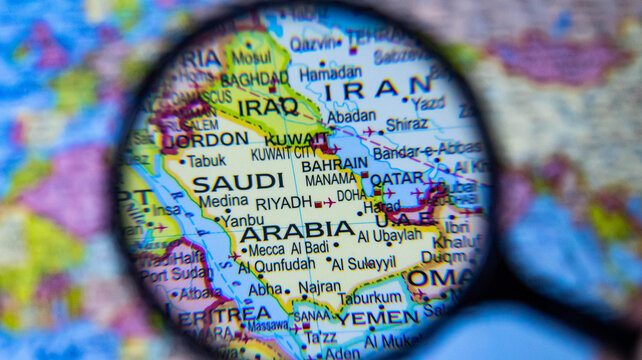 magnifying glass hovering over saudi arabia and its arabian peninsula neighbors on a map.