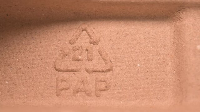 Recycling sign PAP (paper) 21 embossed on brown cardboard packaging texture. Macro shot emphasizing sustainable materials and eco friendly shipping solutions for commercial green marketing campaigns