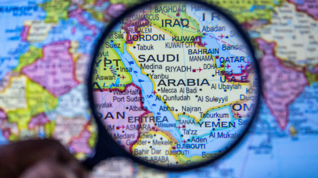 Magnifying glass focused on Saudi Arabia and Middle East region on world map.