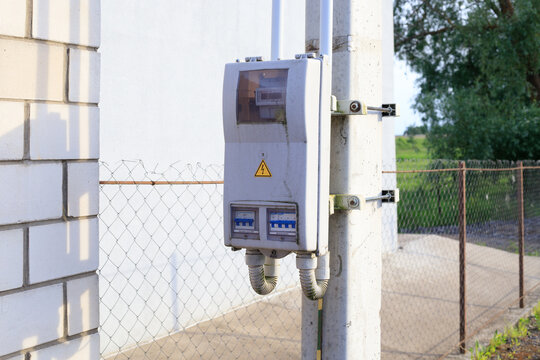 Outdoor electric meter box with high voltage warning sign on concrete pole, electrical switchboard and wire fence background