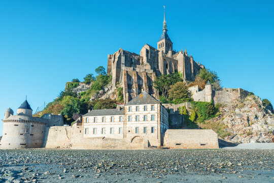 Stone fortifications and medieval abbey of Mont Saint-Michel stand above exposed tidal sands in Normandy, France. Tidal island with gothic cathedral in Normandie. French architecture