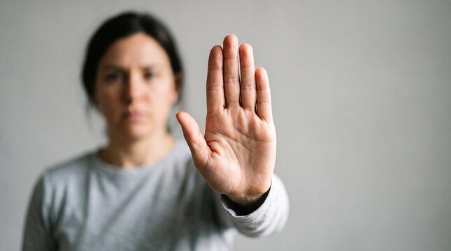 young woman showing stop sign. A powerful, minimalist conceptual portrait of a person extending an open palm directly toward the camera in a universal "stop" gesture, symbolizing personal boundaries.