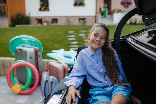 Cute girl sitting in a car trunk and waiting before roadtrip or vacation.