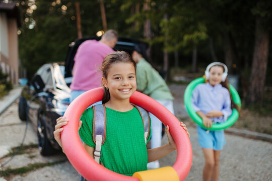 Happy family leaving home for summer vacation with luggage and pool toys.