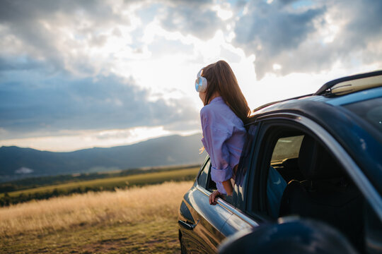 Little girl with headphones standing and leaning out of the car window during the ride.