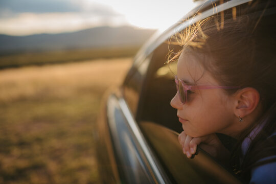 Little girl with sunglasses looking out of the car window during the ride.