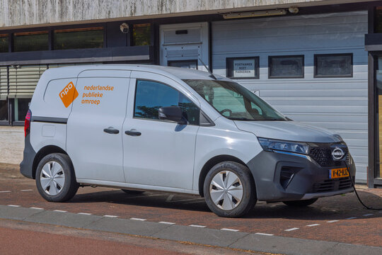 Hilversum, Netherlands - July 13, 2026: A white Nissan electric van branded with the orange NPO Nederlandse Publieke Omroep logo connected to a charging cable outside a building.