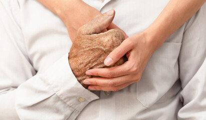 A young woman's arms embrace and hold the hand of an elderly man. Concept of support and care for the elderly. © Ирина Гутыряк