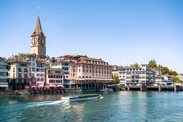 Scenic view of the Limmat River in Zurich, featuring the historic St. Peter church with its prominent clock tower as a focal point, along with a riverboat traveling through the city center. © Agnieszka Gaul
