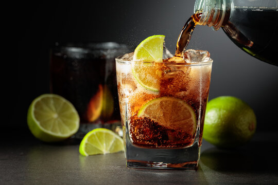 Refreshing cocktail with lime, cola and ice in a glass on a black table.