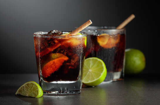 Refreshing cocktail with lime, cola and ice in a glass on a black table.
