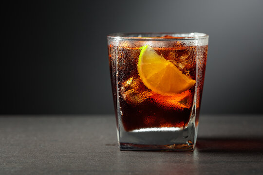 Refreshing cocktail with lime, cola and ice in a glass on a black table.