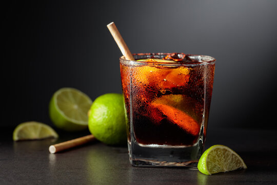 Refreshing cocktail with lime, cola and ice in a glass on a black table.