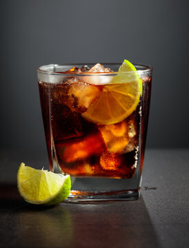 Refreshing cocktail with lime, cola and ice in a glass on a black table.