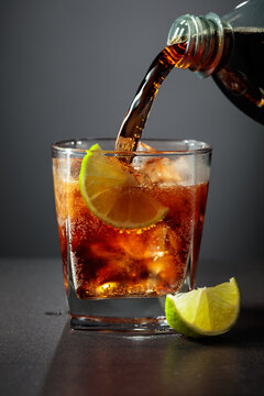 Refreshing cocktail with lime, cola and ice in a glass on a black table.