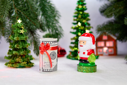 Santa Claus with a decorated dollar bill against a background of Christmas trees with a house and a car
