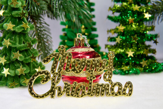 Letters and a red ball with golden patterns on a background of Christmas trees