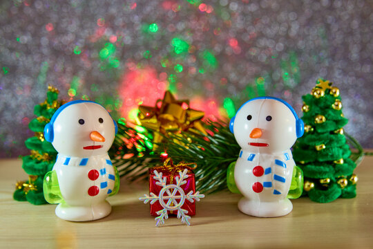 Unusual snowmen and a snowflake with a gift near a Christmas tree branch and fir trees on a gray background