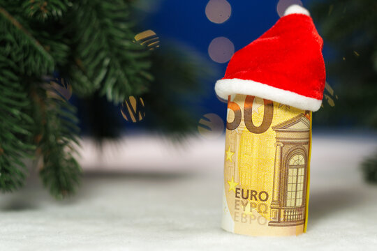 A euro banknote with a Santa Claus hat on a white background with green fir trees