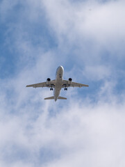 Fototapeta premium Commercial Passenger Airplane Flying Overhead Against Blue Sky During Landing Approach