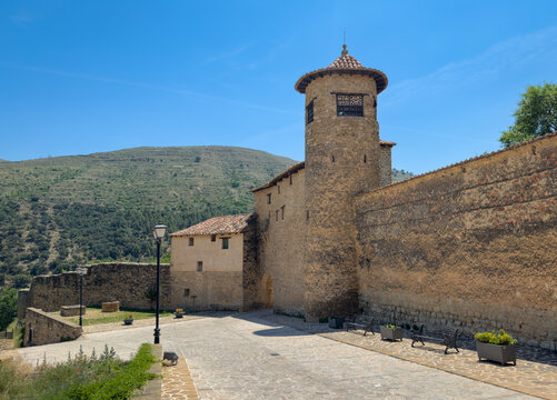 Cylindrical stone watchtower with conical tiled roof rising above the medieval defensive walls of Mirambel village, Teruel, Aragon, Spain, with green mountains behind