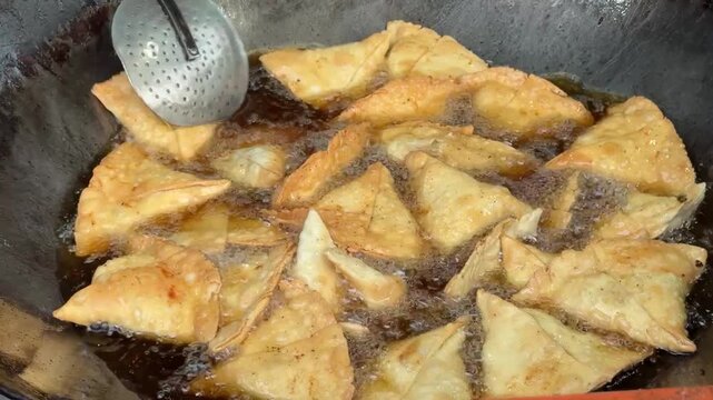 Traditional Pakistani samosas being deep-fried in hot oil inside a large iron wok (karahi) at a local street food stall. The crispy, golden pastries are freshly prepared and cooked to perfection, show